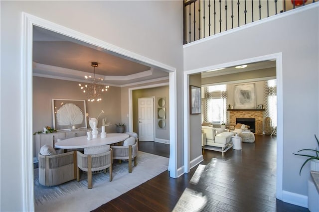 dining space featuring a raised ceiling, a fireplace, dark hardwood / wood-style floors, and an inviting chandelier