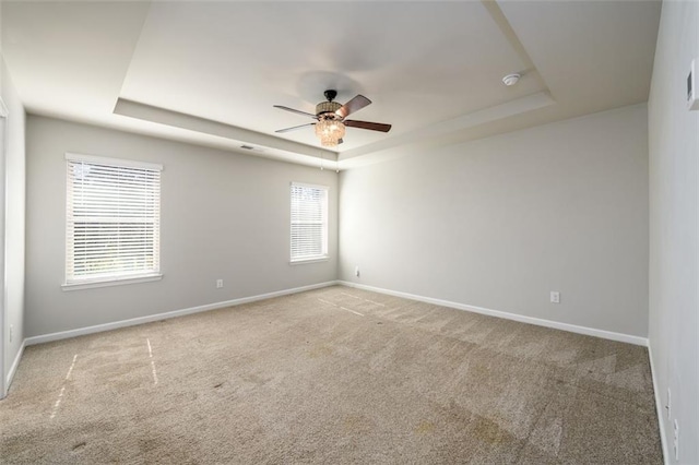 carpeted spare room featuring ceiling fan, a tray ceiling, and baseboards