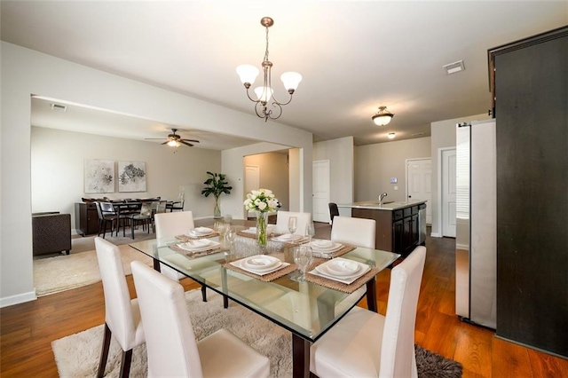 dining space with dark wood-style floors, ceiling fan with notable chandelier, visible vents, and baseboards