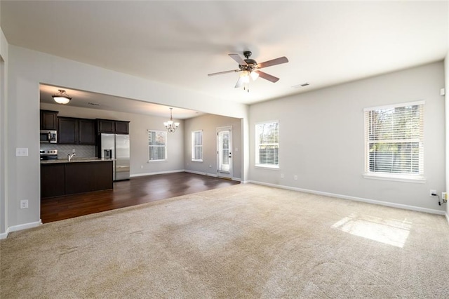 unfurnished living room featuring a healthy amount of sunlight, dark colored carpet, and ceiling fan with notable chandelier