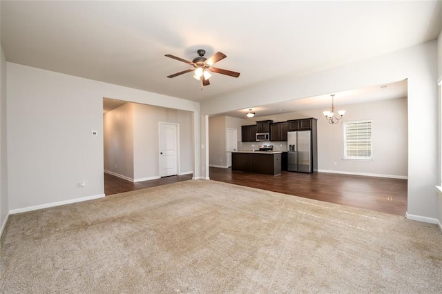 unfurnished living room featuring dark carpet, baseboards, and ceiling fan with notable chandelier