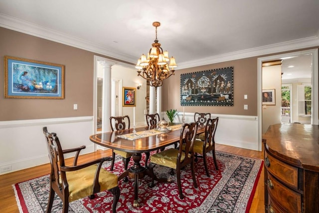 dining space with a notable chandelier, wood-type flooring, ornate columns, and crown molding