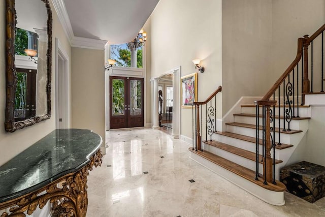 entrance foyer with an inviting chandelier, ornamental molding, a high ceiling, and french doors