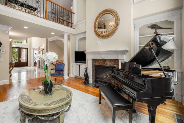 miscellaneous room with french doors, a towering ceiling, decorative columns, hardwood / wood-style flooring, and a fireplace