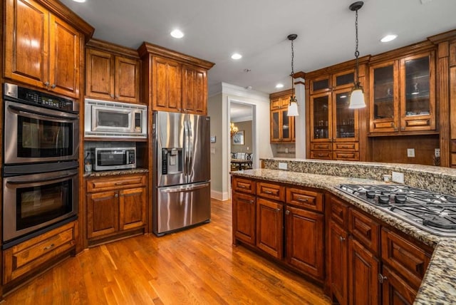 kitchen with wood-type flooring, stainless steel appliances, light stone counters, and pendant lighting