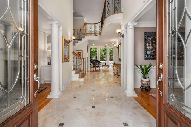 entrance foyer with ornate columns, crown molding, a towering ceiling, and light wood-type flooring