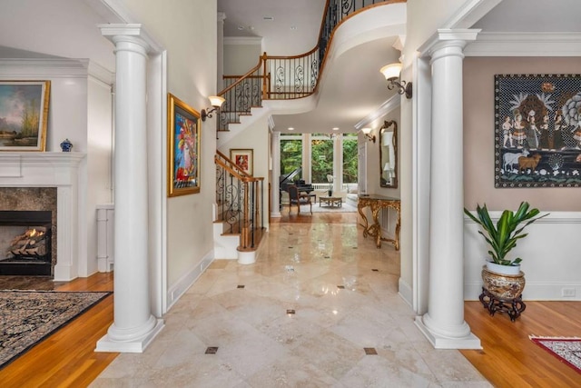 entrance foyer with ornate columns, hardwood / wood-style floors, a high end fireplace, and ornamental molding