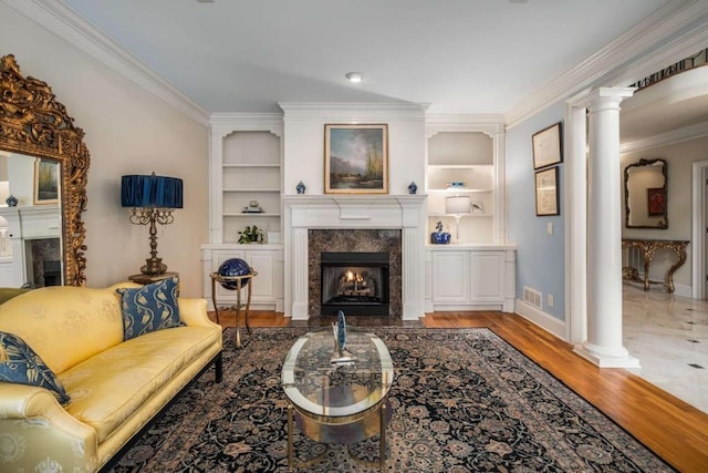 living room with a high end fireplace, crown molding, built in features, light wood-type flooring, and ornate columns