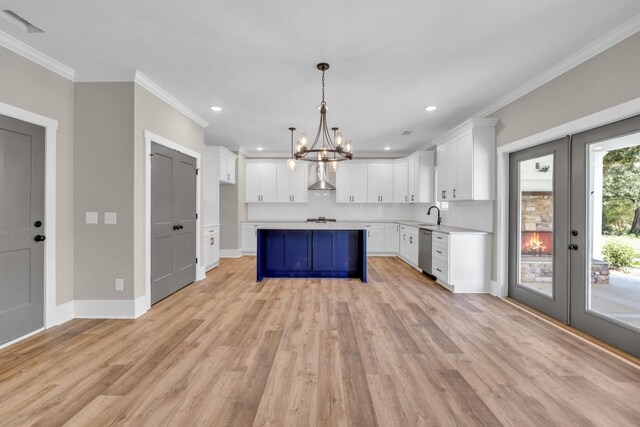 kitchen with light hardwood / wood-style floors, stainless steel dishwasher, white cabinetry, hanging light fixtures, and wall chimney range hood