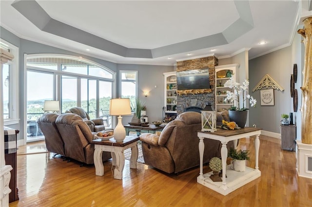 living room with a fireplace, light hardwood / wood-style floors, a raised ceiling, and crown molding