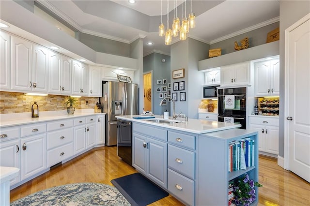 kitchen with decorative backsplash, light wood-type flooring, white cabinets, sink, and a center island with sink