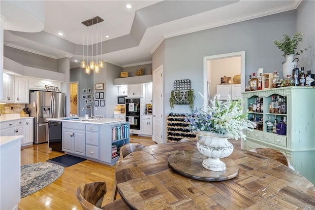 dining space with sink, light hardwood / wood-style flooring, crown molding, and a raised ceiling