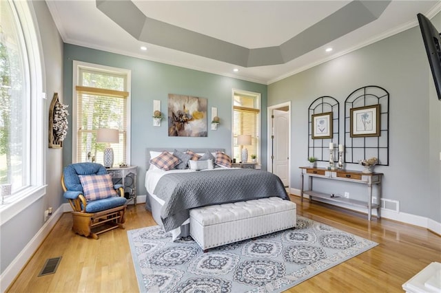 bedroom with light hardwood / wood-style floors, a raised ceiling, and crown molding