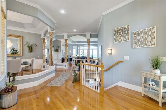 corridor with a tray ceiling, light hardwood / wood-style flooring, decorative columns, and ornamental molding