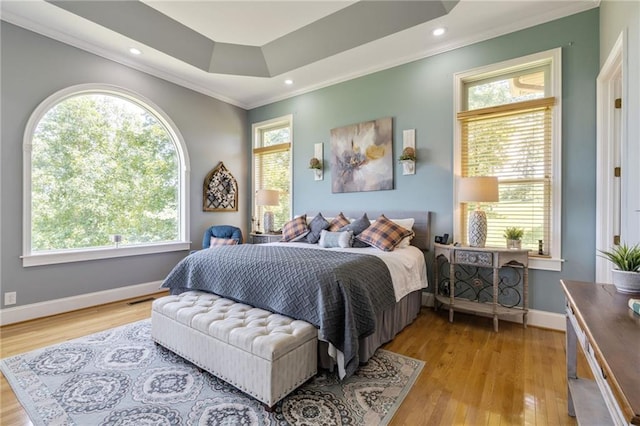 bedroom with a tray ceiling, multiple windows, and light hardwood / wood-style flooring