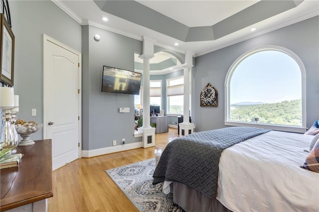 bedroom with decorative columns, crown molding, light wood-type flooring, and a tray ceiling