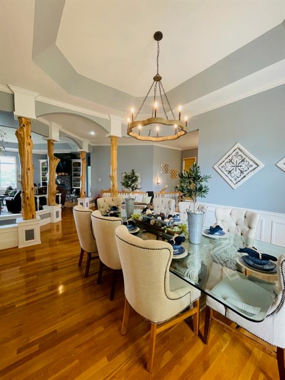 dining area featuring a chandelier, ornate columns, hardwood / wood-style floors, and a raised ceiling