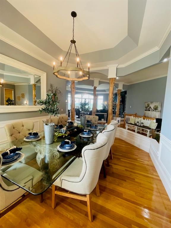 dining space with decorative columns, a chandelier, a raised ceiling, and light hardwood / wood-style floors