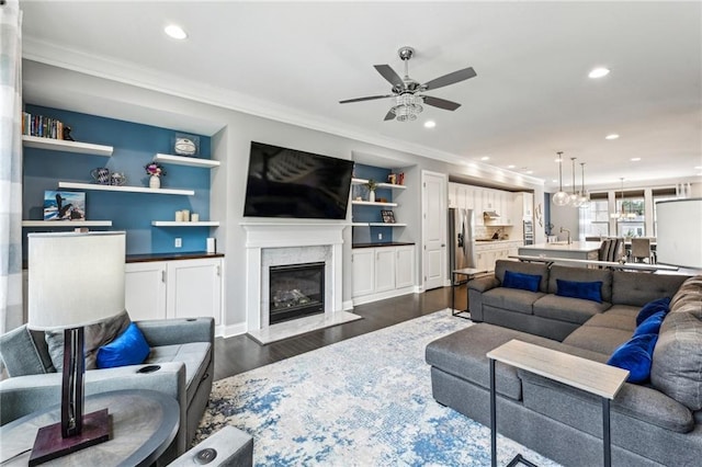 living room with a high end fireplace, dark wood-style floors, ornamental molding, built in shelves, and recessed lighting