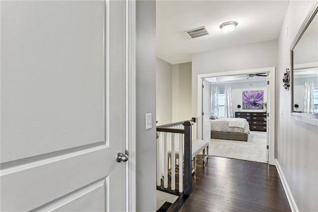 hall with dark wood-style floors, baseboards, visible vents, and an upstairs landing