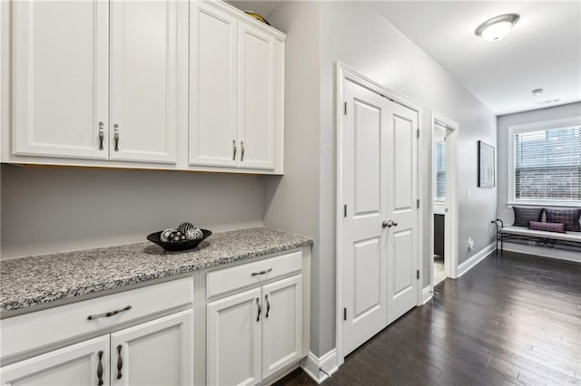 interior space featuring baseboards, white cabinetry, light stone counters, and dark wood-style flooring