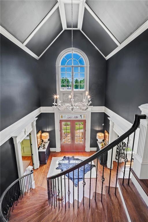 stairway with french doors, vaulted ceiling, a chandelier, and hardwood / wood-style floors