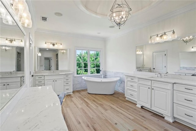 bathroom with tile walls, hardwood / wood-style flooring, vanity, a washtub, and a notable chandelier