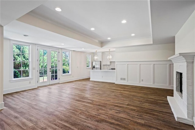 unfurnished living room with wood-type flooring, ornamental molding, a tray ceiling, a brick fireplace, and french doors