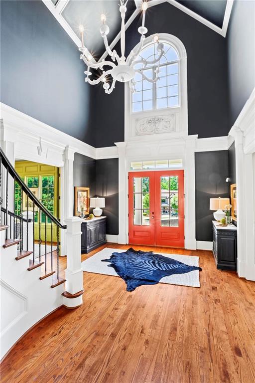 foyer with french doors, an inviting chandelier, wood-type flooring, ornamental molding, and a high ceiling