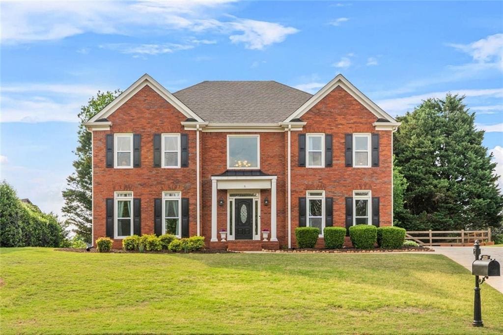 colonial inspired home featuring brick siding, fence, and a front yard