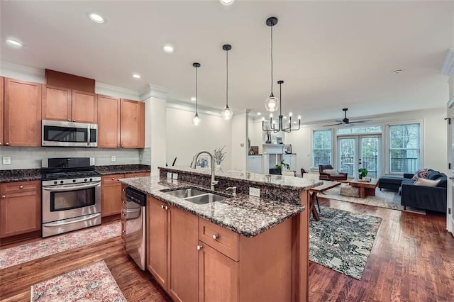 kitchen with sink, decorative light fixtures, appliances with stainless steel finishes, an island with sink, and dark stone counters