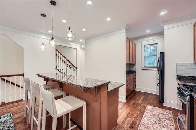 kitchen featuring black refrigerator, dark hardwood / wood-style floors, dark stone counters, hanging light fixtures, and ornamental molding