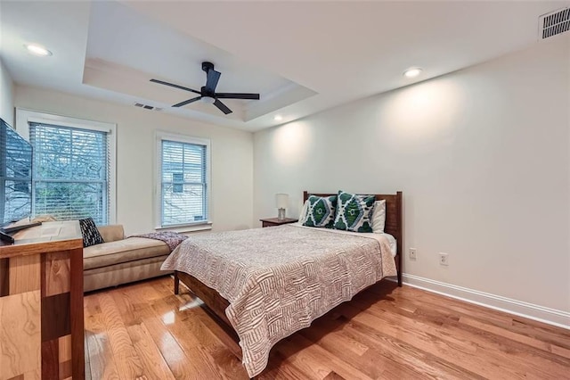 bedroom with ceiling fan, a tray ceiling, and light wood-type flooring