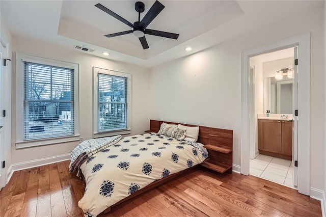 bedroom with hardwood / wood-style flooring, ceiling fan, a tray ceiling, and ensuite bath