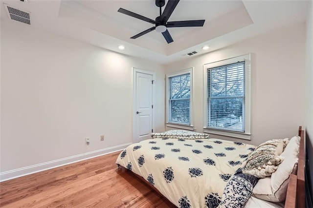 bedroom with a raised ceiling, wood-type flooring, and ceiling fan