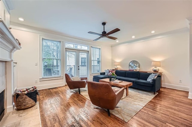 living room with french doors, crown molding, light hardwood / wood-style flooring, ceiling fan, and a tiled fireplace