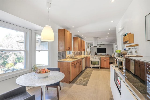 kitchen featuring island exhaust hood, appliances with stainless steel finishes, a peninsula, brown cabinetry, and decorative backsplash