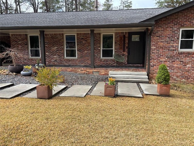 view of exterior entry featuring a yard, brick siding, and covered porch