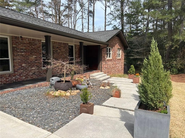 exterior space featuring brick siding and roof with shingles