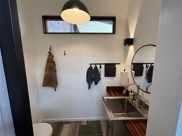 bathroom with toilet, wood finished floors, baseboards, and a sink