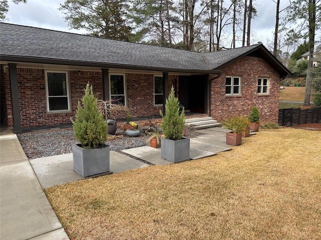 single story home featuring a front yard, fence, brick siding, and roof with shingles