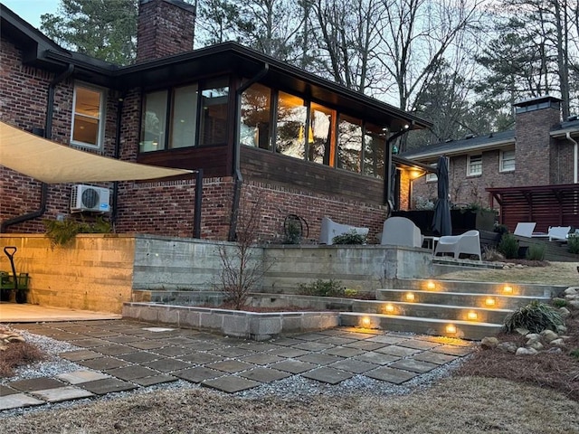 back of house featuring brick siding, a chimney, and a sunroom