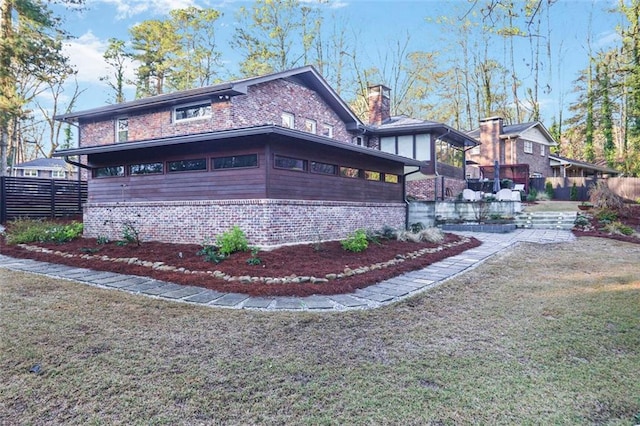 view of home's exterior featuring brick siding, a lawn, a chimney, and fence