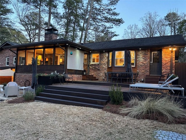 rear view of house with brick siding, a deck, a chimney, and entry steps