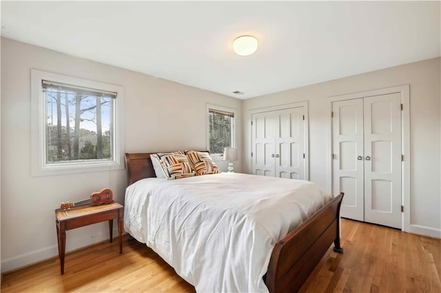 bedroom with multiple closets, baseboards, multiple windows, and light wood finished floors