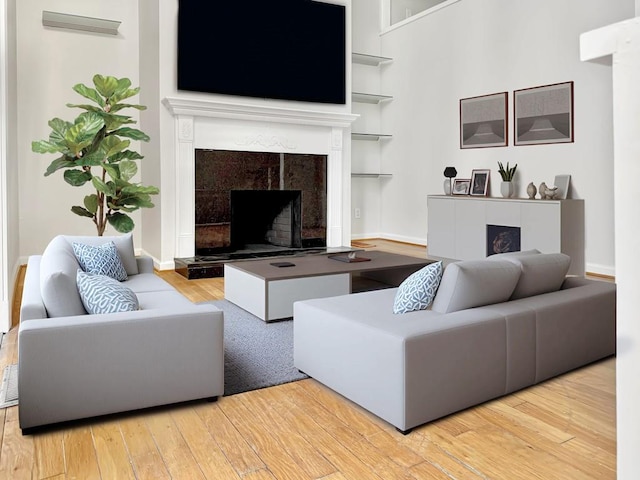 living room featuring built in shelves, wood finished floors, a high end fireplace, and baseboards