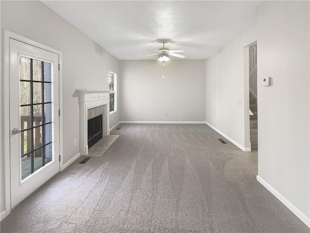 unfurnished living room featuring a ceiling fan, baseboards, stairs, a tiled fireplace, and carpet flooring