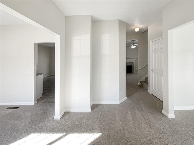 empty room with visible vents, a ceiling fan, a fireplace, carpet flooring, and baseboards