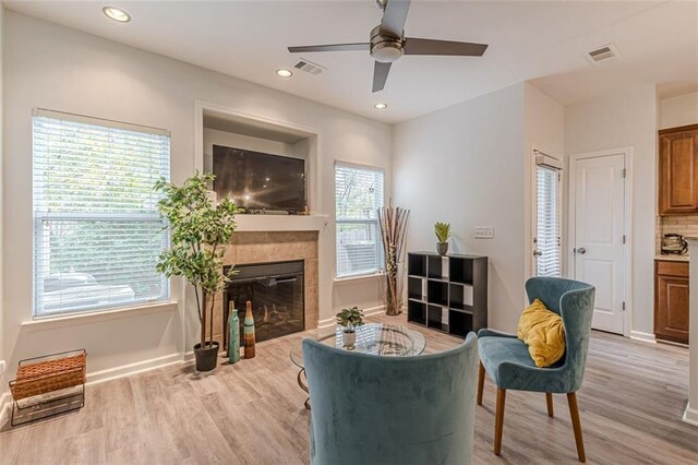 sitting room with a fireplace, a wealth of natural light, ceiling fan, and light wood-type flooring