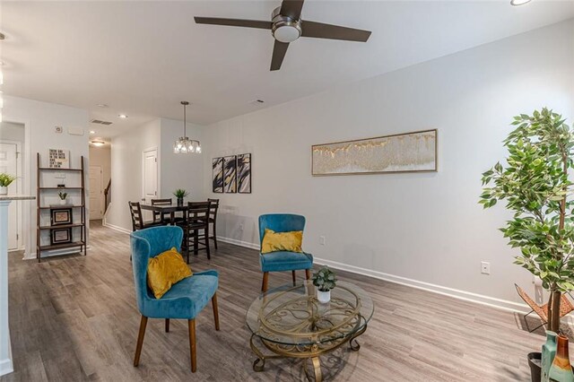 sitting room with hardwood / wood-style floors and ceiling fan with notable chandelier